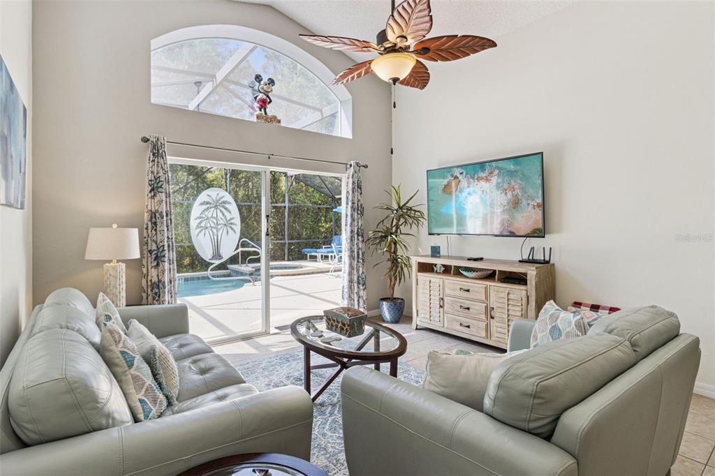 A living room features light-colored sofas, a television, a ceiling fan, and a pool view — 138 MADIERA BEACH BOULEVARD, KISSIMMEE, FL