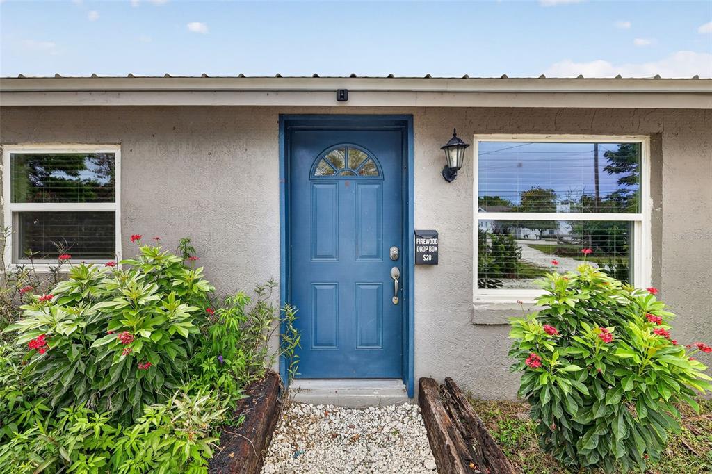 A blue front door with a firewood drop box is centered on a stucco exterior wall — 1111 DORA AVENUE, TAVARES, FL