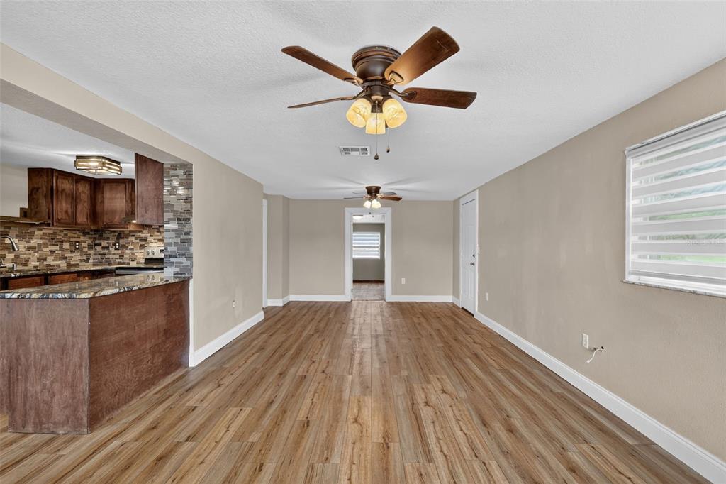 A living room with wood-look flooring, a ceiling fan, and an open view into the kitchen — 1111 DORA AVENUE, TAVARES, FL
