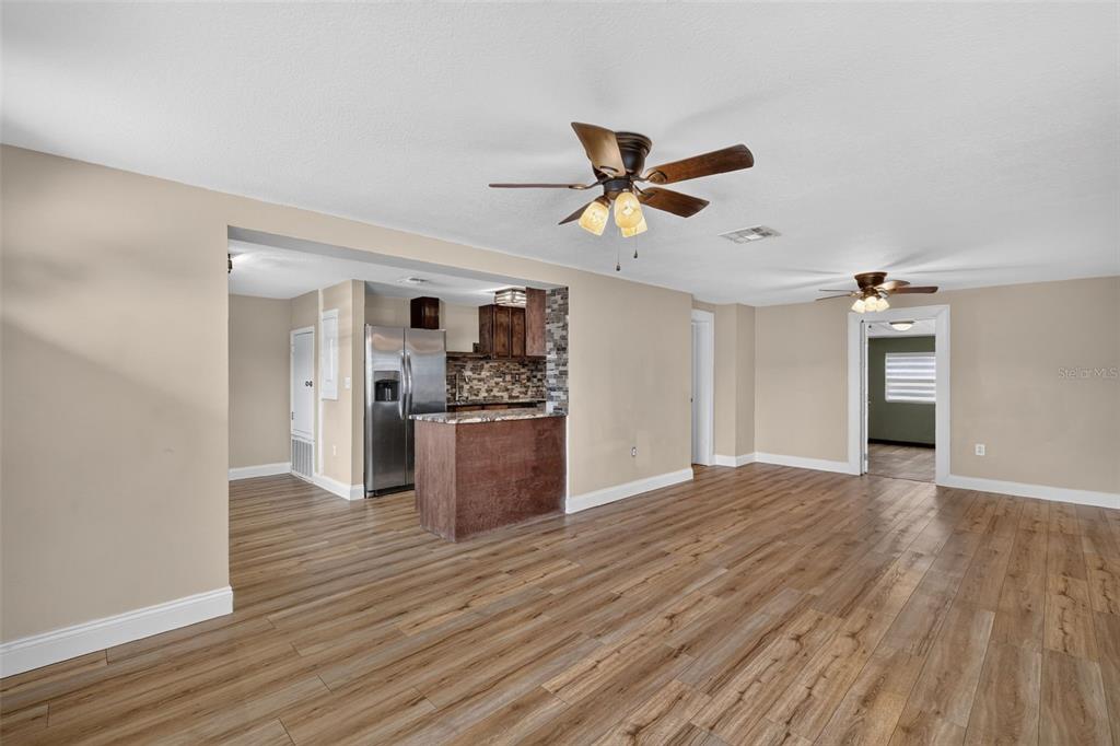 An open-concept living area with wood-look flooring, a ceiling fan, and an adjacent kitchen — 1111 DORA AVENUE, TAVARES, FL