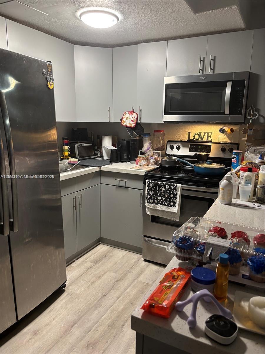 A compact kitchen features gray cabinets, stainless steel appliances, and light wood-look flooring — 16450 NW 2nd Ave # 109, Miami FL 33169, MIAMI, FL