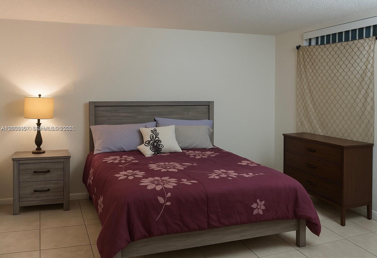 A bedroom features a bed with a floral comforter, a nightstand, and a wooden dresser — 16450 NW 2nd Ave # 109, Miami FL 33169, MIAMI, FL