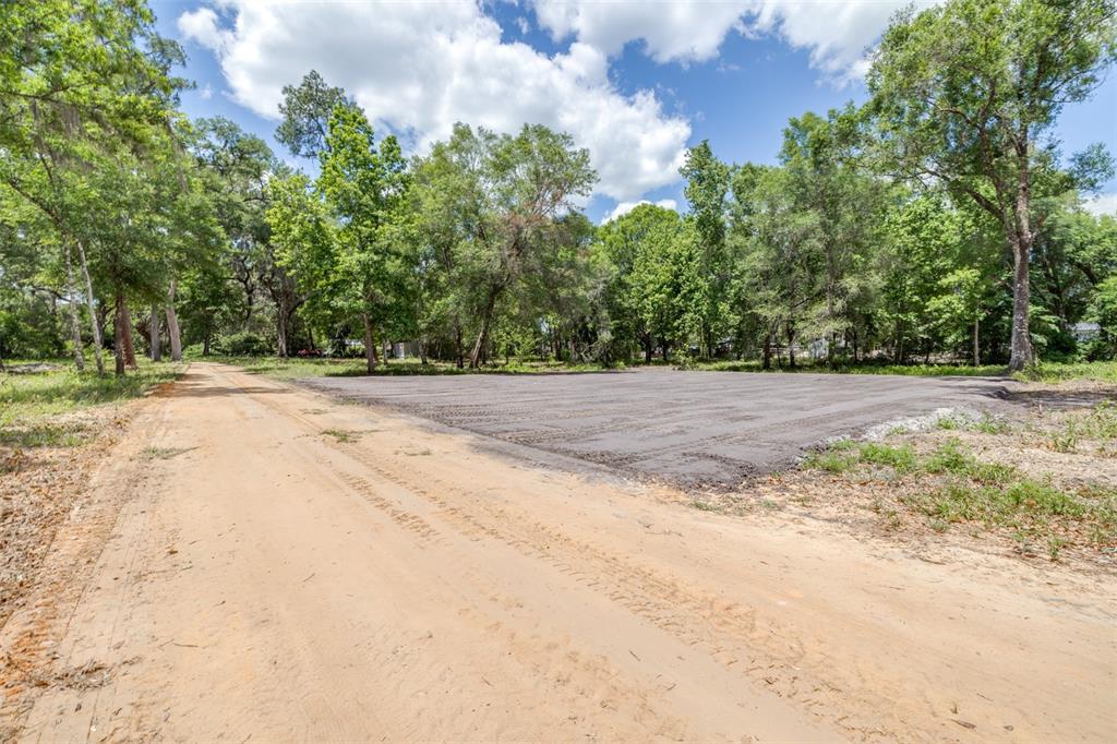A dirt road runs alongside a cleared, leveled rectangular plot of land surrounded by trees — SE 124TH AVENUE, WEBSTER, FL