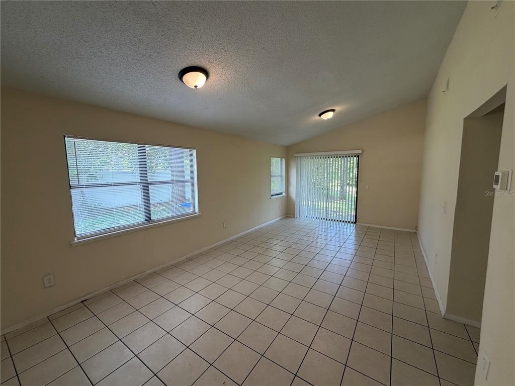 An empty living room features beige tile flooring, vaulted ceilings, and a sliding glass door — 11608 ANJALI COURT, ORLANDO, FL