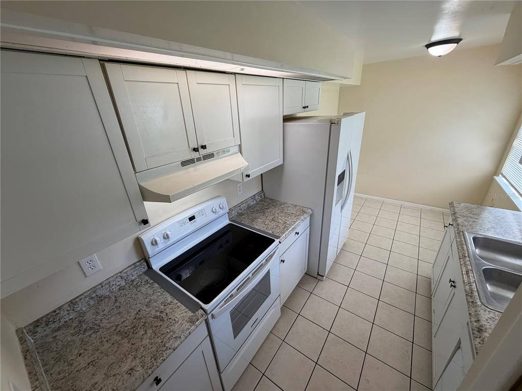 A narrow kitchen features white cabinets, granite countertops, a white stove, and tiled flooring — 11608 ANJALI COURT, ORLANDO, FL