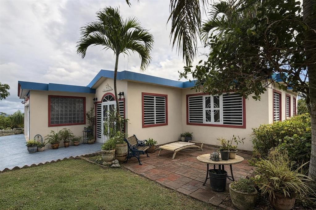 A single-story house with a tiled patio, palm tree, and red-trimmed windows under a cloudy sky — KM 2.4 CAMINO ALGARROBO BUENA VISTA WARD, BAYAMON, PR