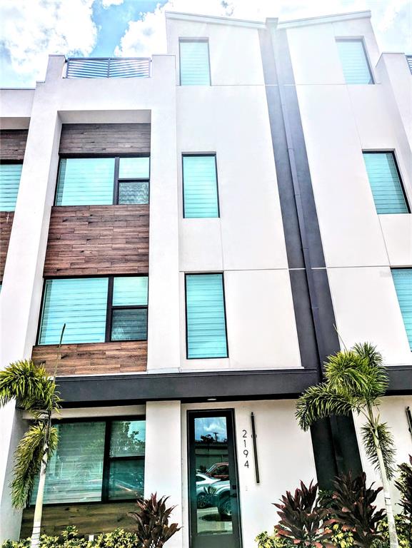 A modern three-story townhouse exterior features white walls, wood-paneled accents, and large rectangular windows — 2194 FRUITVILLE ROAD, SARASOTA, FL