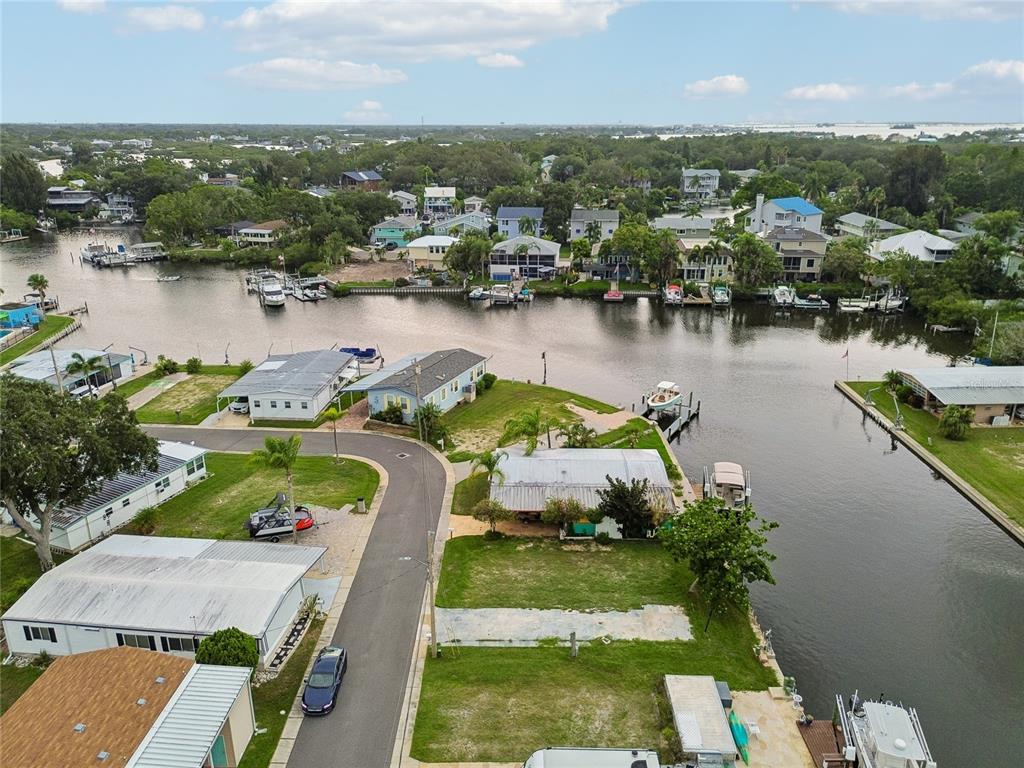 An aerial view shows waterfront homes along a canal with private docks and parked boats — 102 SCHOONER DRIVE UNIT 102, PALM HARBOR, FL