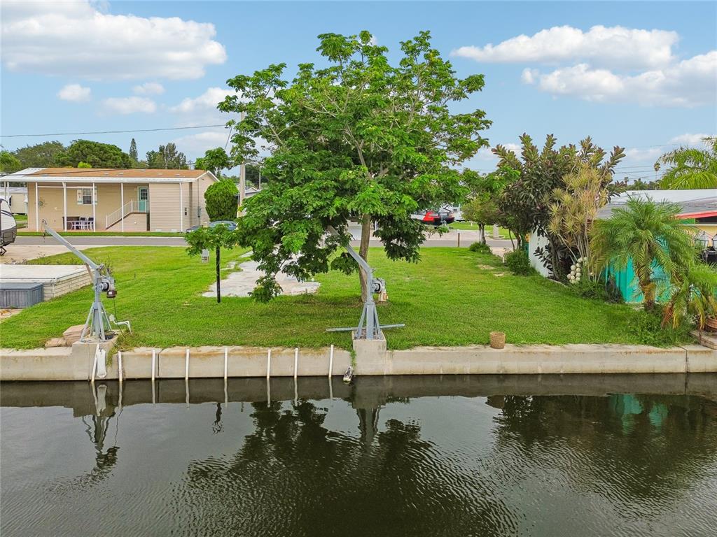 A grassy waterfront lot features a large tree, two boat lifts, and a concrete seawall — 102 SCHOONER DRIVE UNIT 102, PALM HARBOR, FL