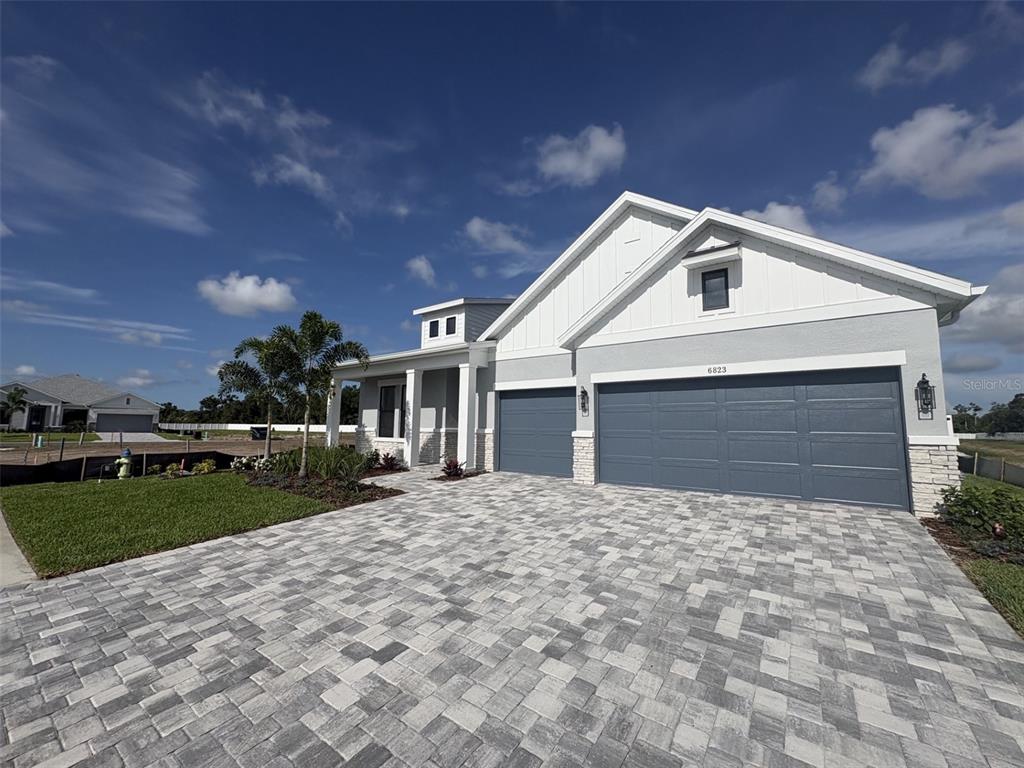 A modern single-story house features a gray garage, white siding, and a paved driveway — 6823 HERON MEADOW DRIVE, SARASOTA, FL