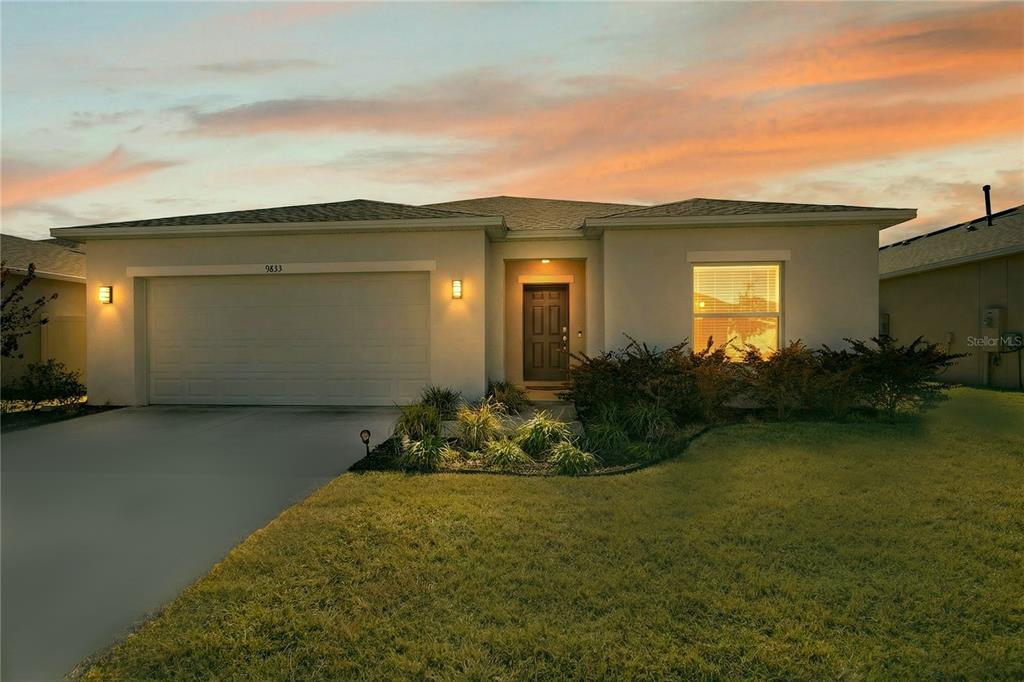 A single-story suburban house with a two-car garage and a landscaped front yard at sunset — 9633 RAMPART ROAD, LEESBURG, FL