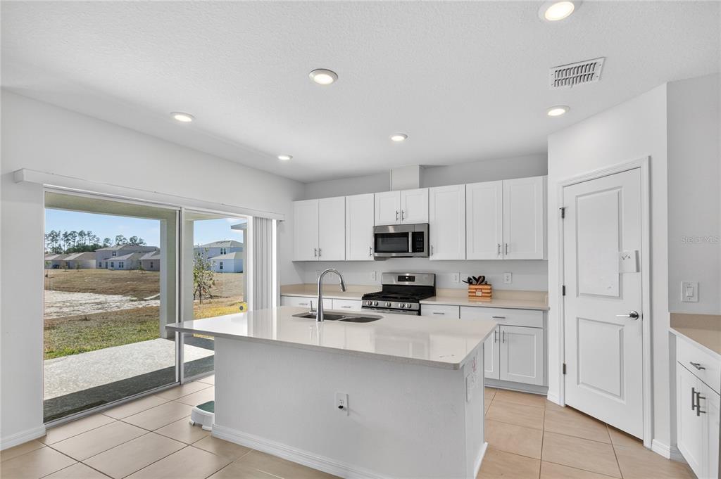 A bright kitchen features white cabinets, quartz countertops, a center island, and sliding glass doors — 9633 RAMPART ROAD, LEESBURG, FL