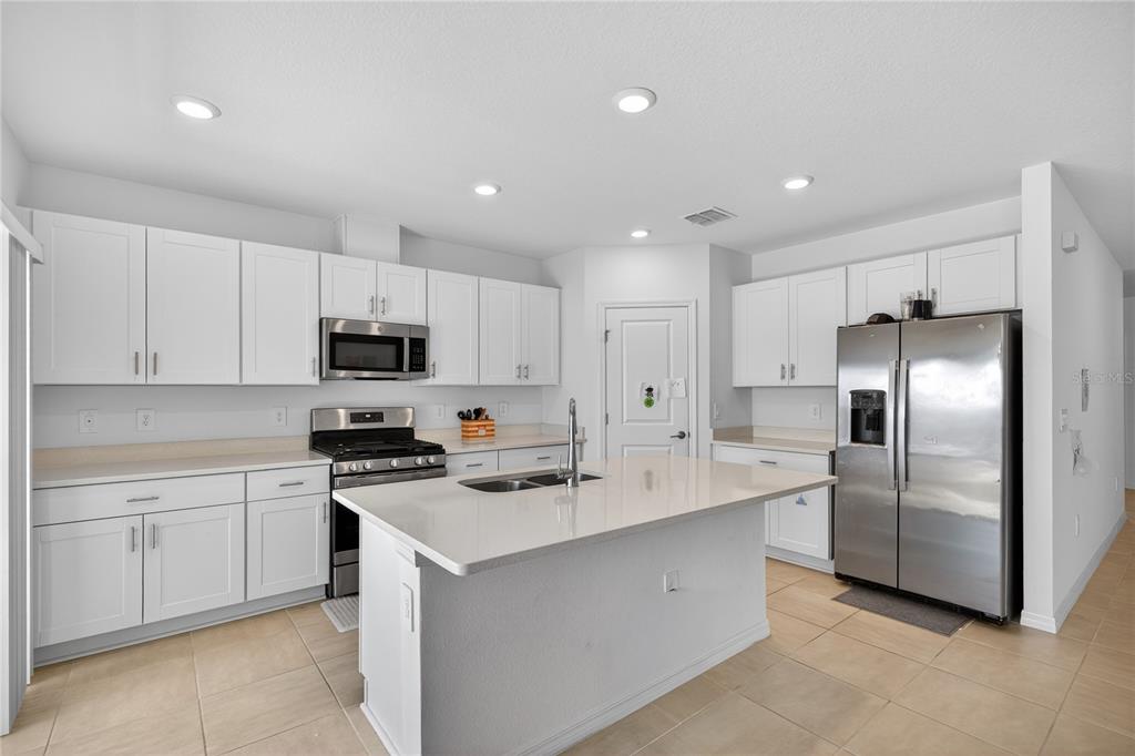 A kitchen features white cabinets, stainless steel appliances, a center island, and tile flooring — 9633 RAMPART ROAD, LEESBURG, FL