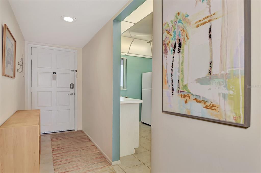 An entryway with a white door, a wooden console table, and a view into a kitchen — 260 SANTA MARIA STREET UNIT 311, VENICE, FL