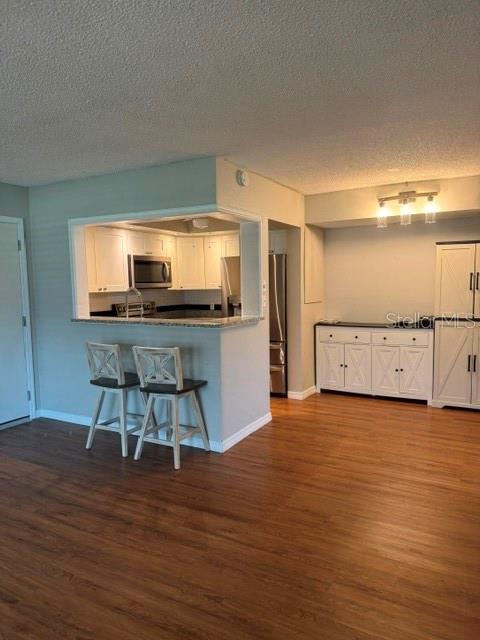A kitchen with a breakfast bar, two stools, and white cabinetry opens to a dining area — 4743 JASPER DRIVE UNIT 101, NEW PORT RICHEY, FL