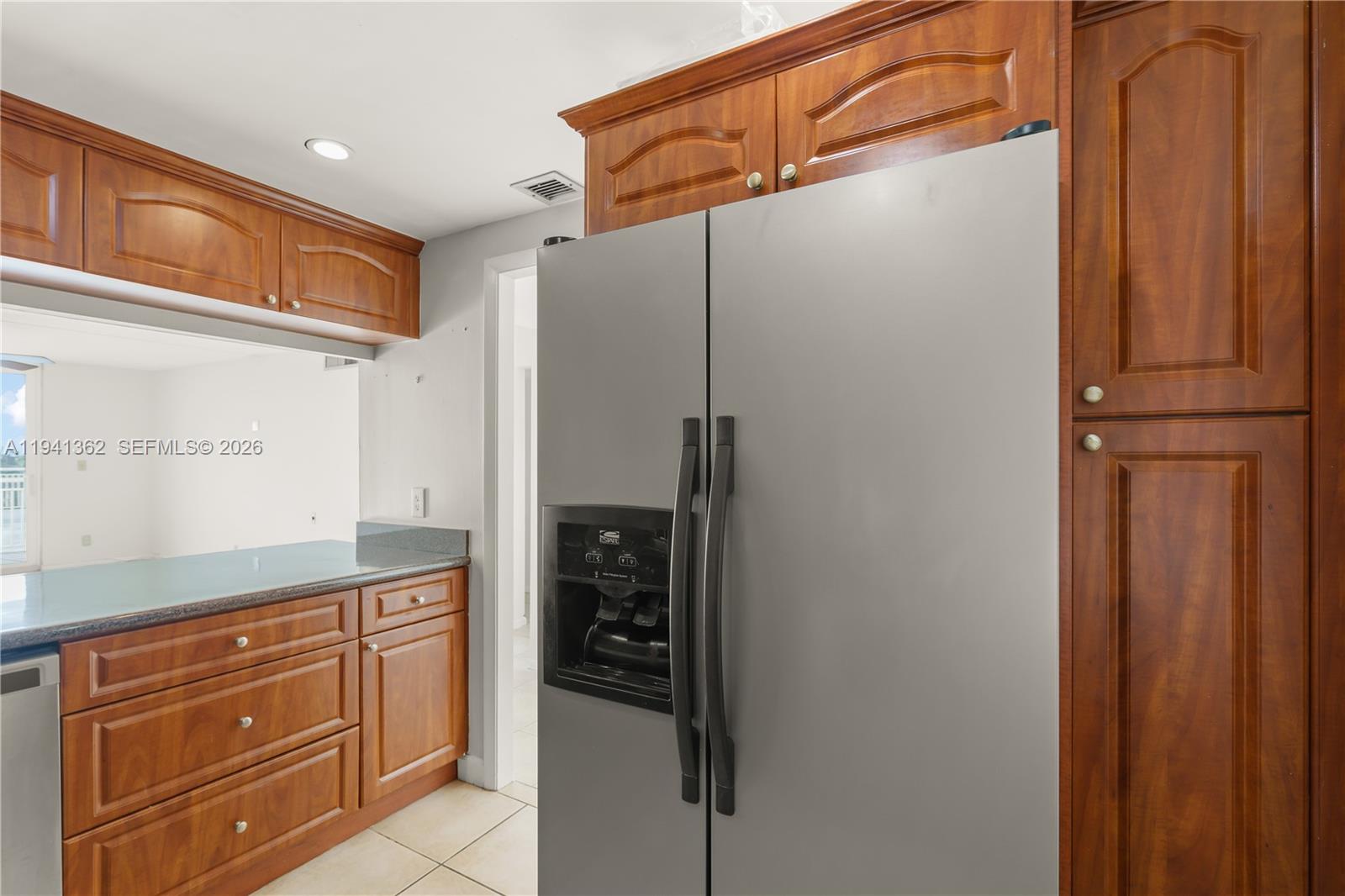 A kitchen features wooden cabinets, a stainless steel refrigerator, and a dark countertop — 437 Golden Isles Dr # 4D, Hallandale Beach FL 33009, HALLANDALE BEACH, FL