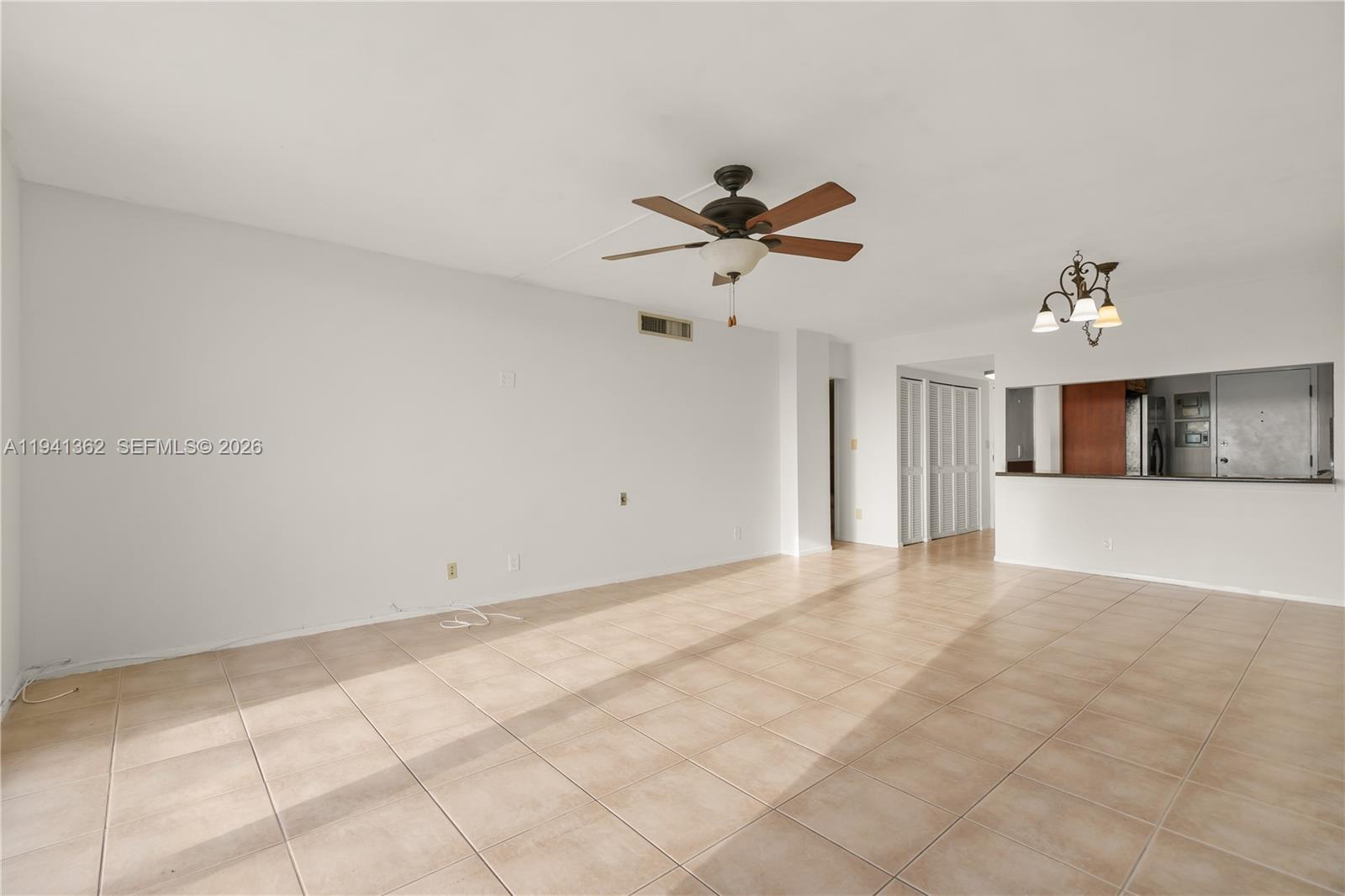 An empty living room features beige tile flooring, a ceiling fan, and a kitchen pass-through — 437 Golden Isles Dr # 4D, Hallandale Beach FL 33009, HALLANDALE BEACH, FL
