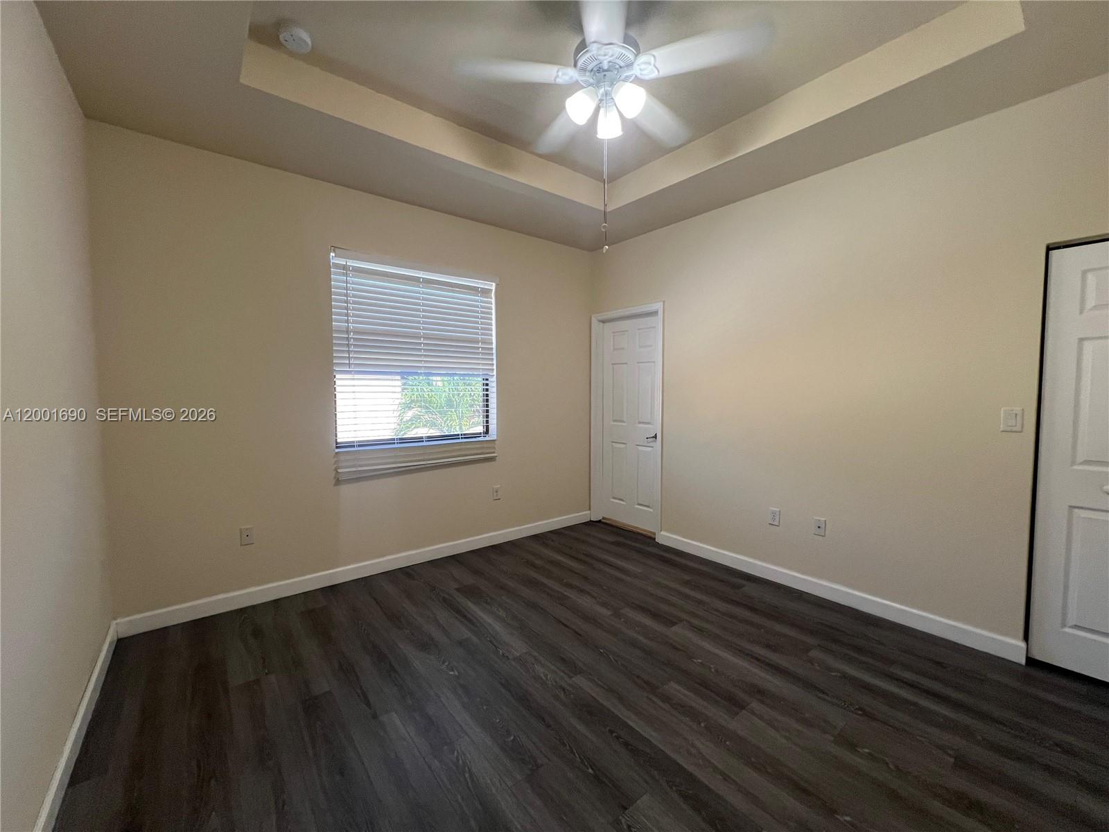 An empty room features dark wood-look flooring, beige walls, a tray ceiling, and a fan — 8913 W 35th Way, Hialeah FL 33018, HIALEAH, FL