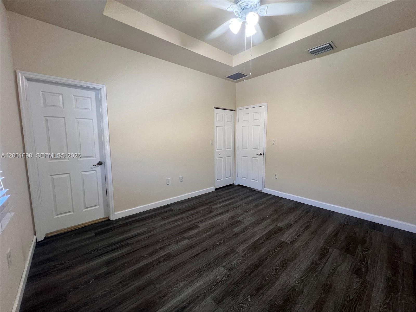An empty room features a tray ceiling, a ceiling fan, and dark wood-look flooring — 8913 W 35th Way, Hialeah FL 33018, HIALEAH, FL
