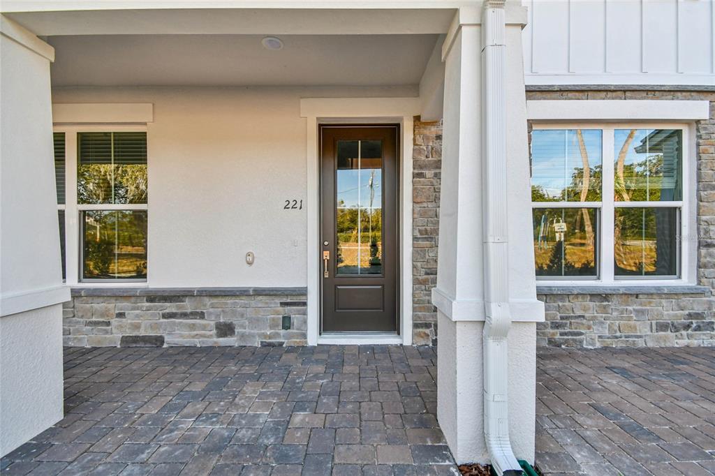 A covered front porch features stone veneer accents, a brown glass-paneled door, and paver flooring — 221 PASQUALA UNIT 18, OVIEDO, FL