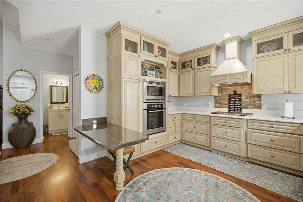 A kitchen features cream-colored cabinetry, stainless steel appliances, a stone backsplash, and dark wood flooring — 1118 AVENIDA DE LAS CASAS, LADY LAKE, FL