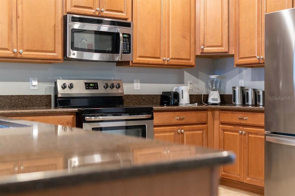 A kitchen features wood cabinets, stainless steel appliances, and dark granite countertops — 1474 ROLLING FAIRWAY DRIVE, DAVENPORT, FL