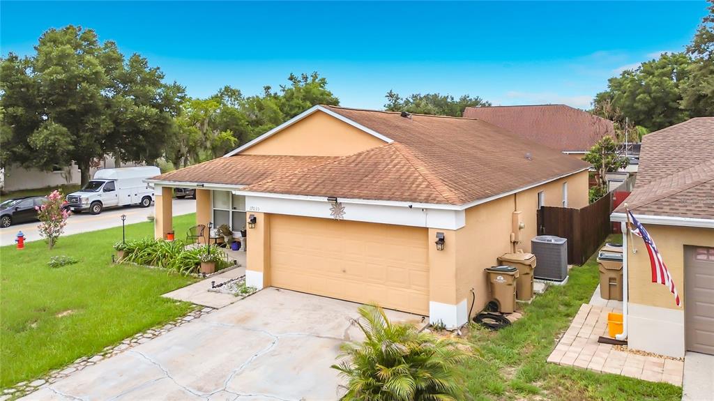 An exterior view of a tan, single-story house with a two-car garage and a driveway — 17035 WOODCREST WAY, CLERMONT, FL