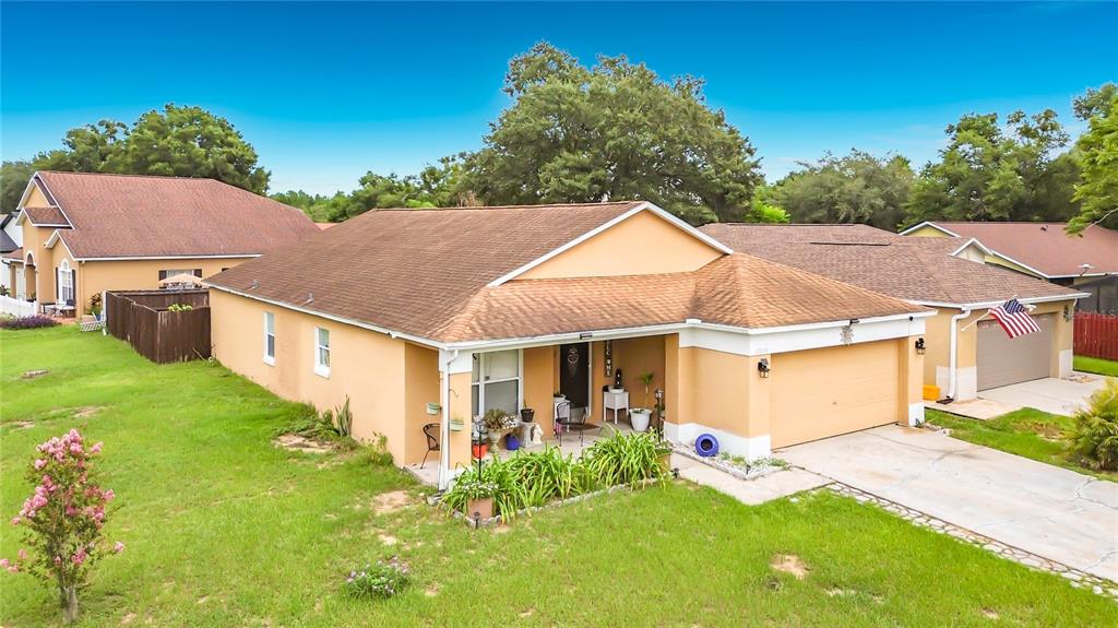 An exterior view of a single-story tan house with a two-car garage and front yard — 17035 WOODCREST WAY, CLERMONT, FL