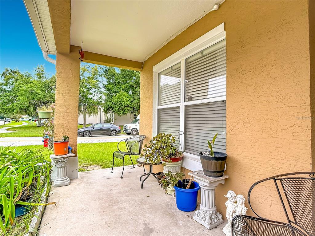 A covered concrete porch features potted plants, metal chairs, and a window with blinds — 17035 WOODCREST WAY, CLERMONT, FL