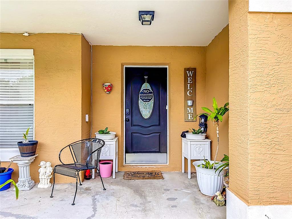 A covered front porch features a dark door, a metal chair, and several potted plants — 17035 WOODCREST WAY, CLERMONT, FL