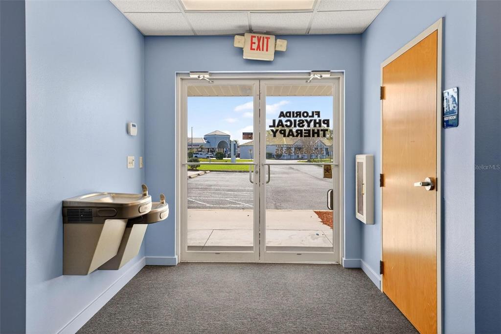 A hallway features a water fountain, an exit door with glass panels, and a restroom door — 17809 SE 109TH AVENUE, SUMMERFIELD, FL