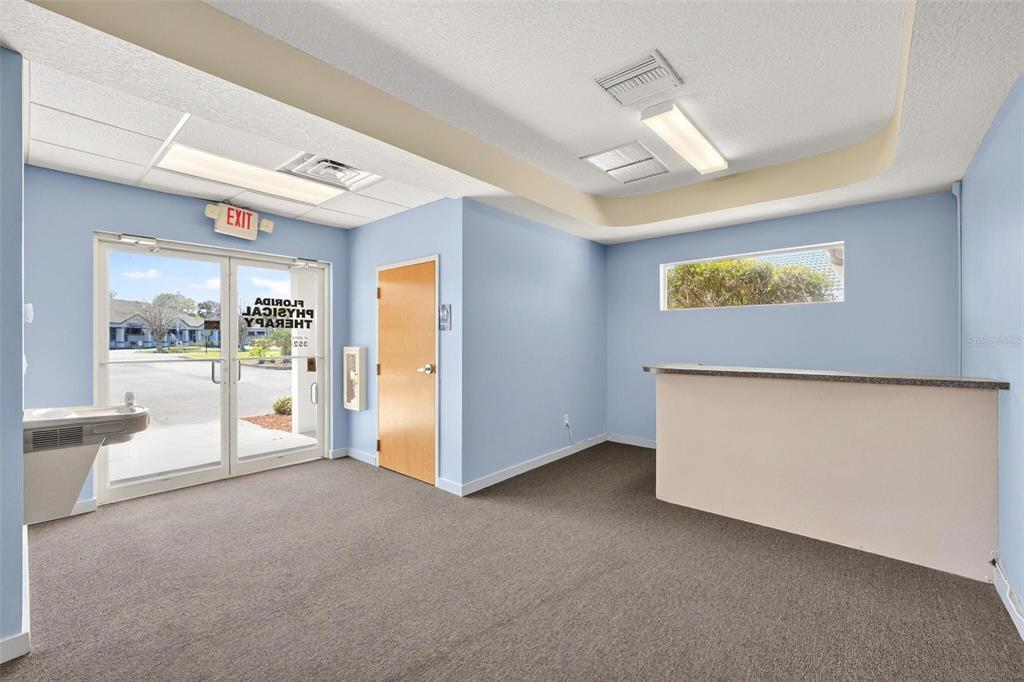 An empty office reception area features light blue walls, gray carpeting, and a service counter — 17809 SE 109TH AVENUE, SUMMERFIELD, FL