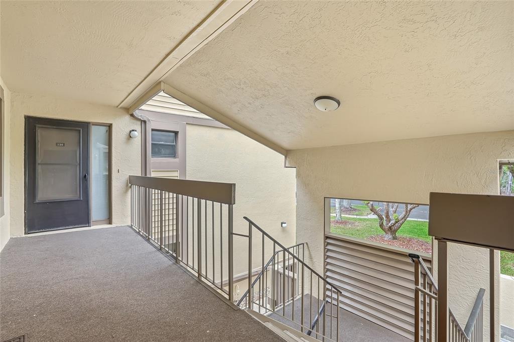 An exterior view of an apartment building landing with stairs, a metal railing, and carpet — 130 WOODLAKE WYNDE UNIT 130, OLDSMAR, FL