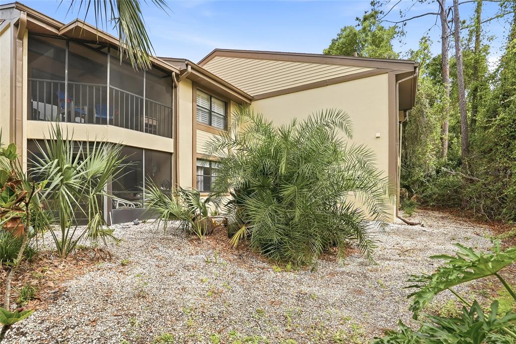 The exterior of a two-story building features screened-in balconies and a gravel yard with palms — 130 WOODLAKE WYNDE UNIT 130, OLDSMAR, FL