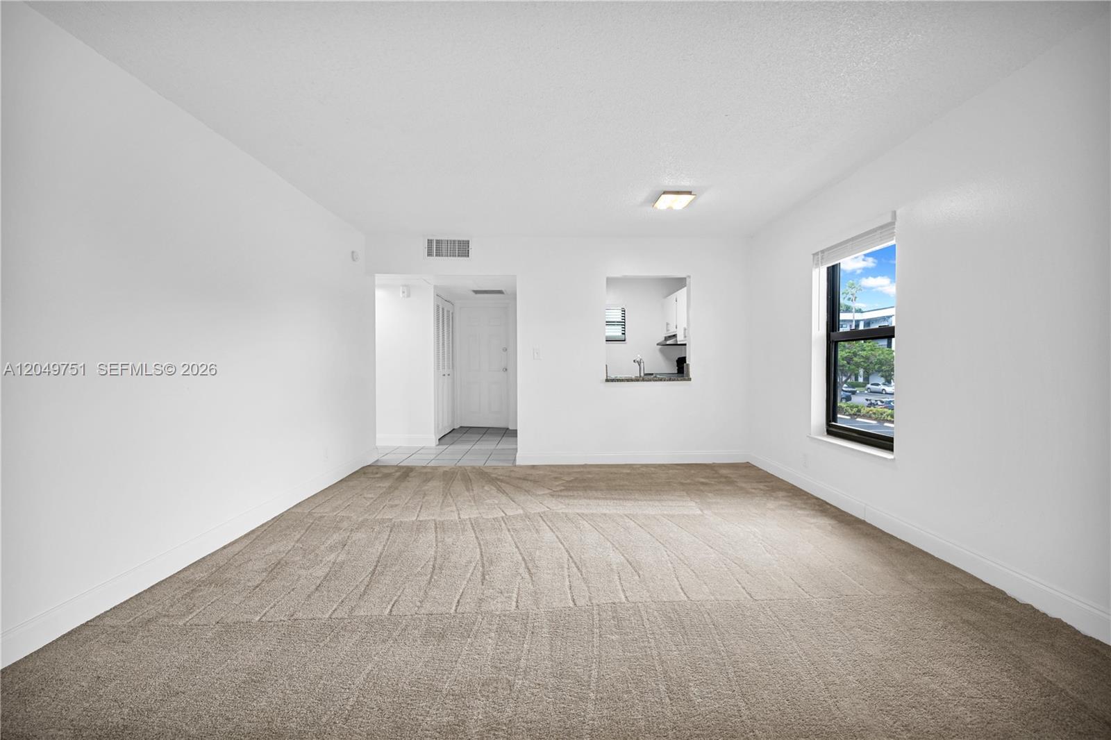 An empty room with beige carpet, white walls, and a pass-through window to the kitchen — 7550 Stirling Rd # V107, Davie FL 33024, DAVIE, FL