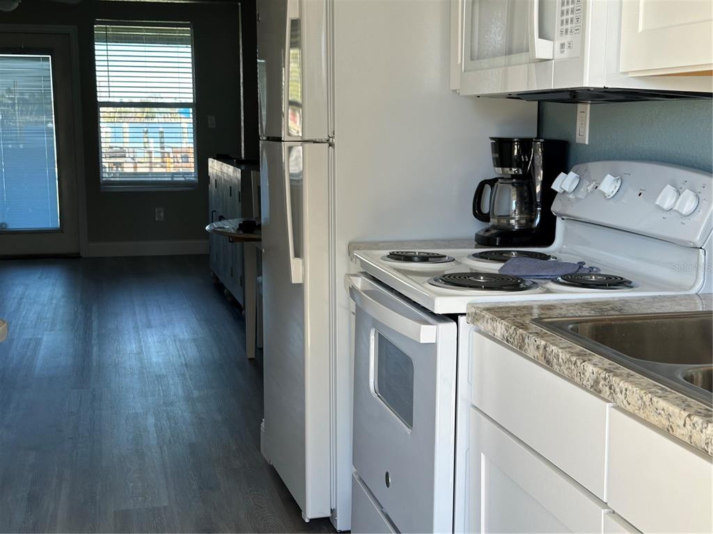 A kitchen features white appliances, a coffee maker, and light countertops, opening to a living area — 5297 S CHEROKEE WAY UNIT 104, HOMOSASSA, FL