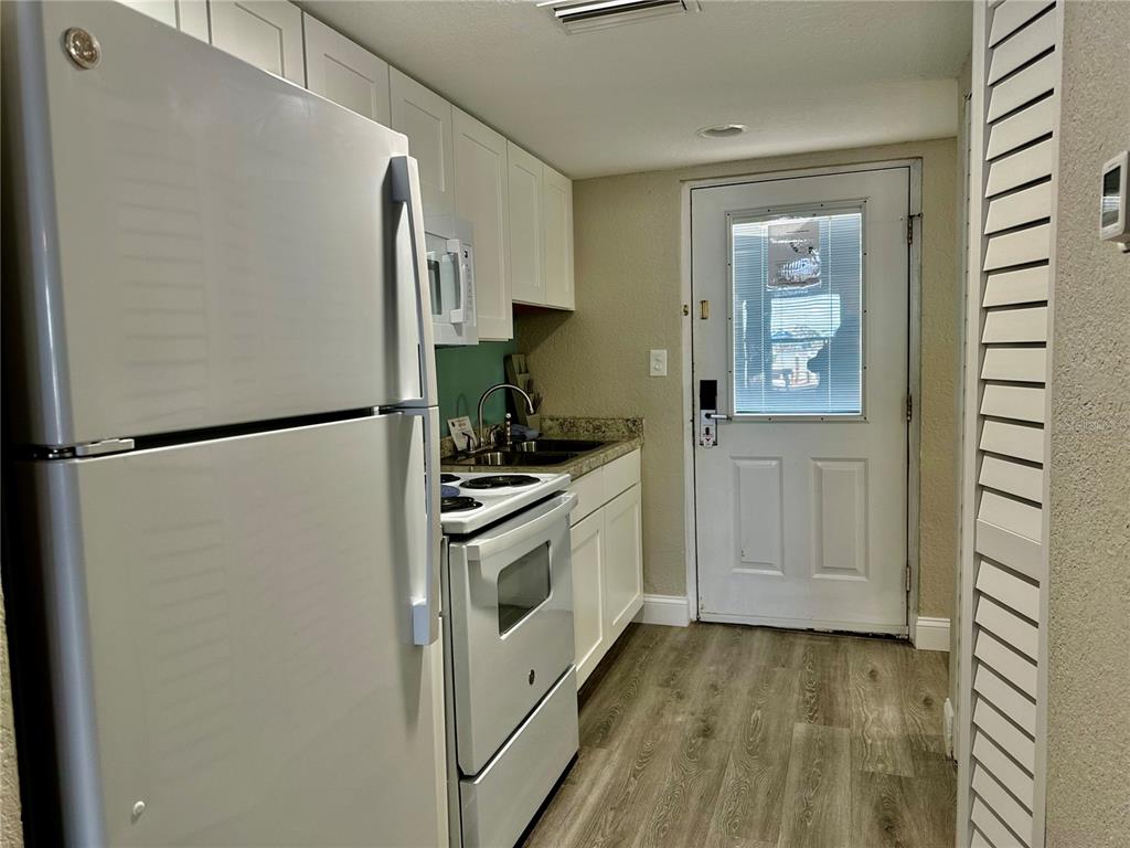 A small kitchen features white cabinets, white appliances, granite countertops, and wood-look flooring — 5297 S CHEROKEE WAY UNIT 104, HOMOSASSA, FL