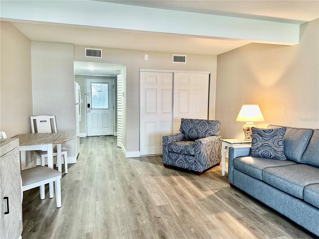 A living room with light wood-look flooring, a blue sofa, an armchair, and a dining area — 5297 S CHEROKEE WAY UNIT 104, HOMOSASSA, FL