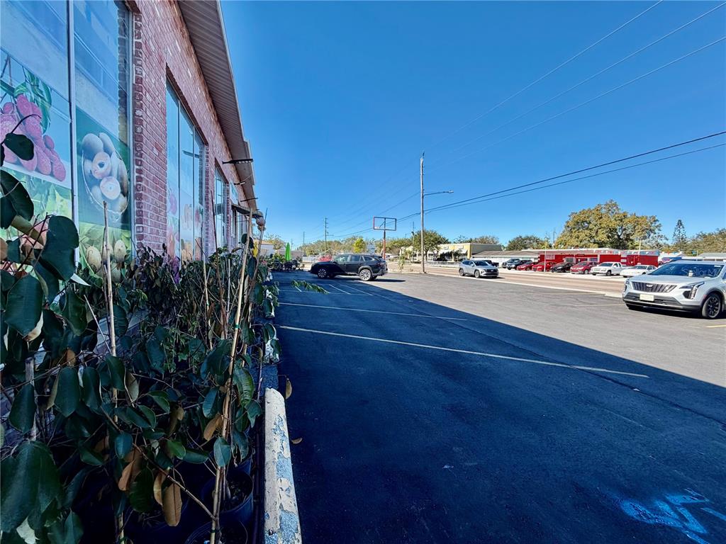 A parking lot sits beside a brick building with large window advertisements and potted plants — 4022 54TH AVENUE N, ST PETERSBURG, FL