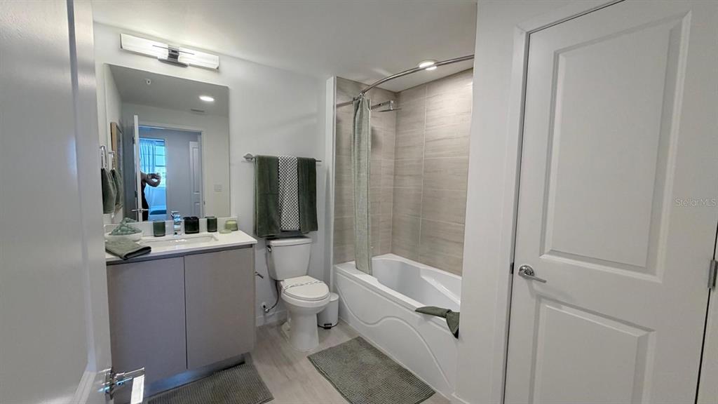 A bathroom features a vanity, a toilet, and a shower-tub combination with tiled walls — 5587 MILLENIA PARK BLVD UNIT 210, ORLANDO, FL