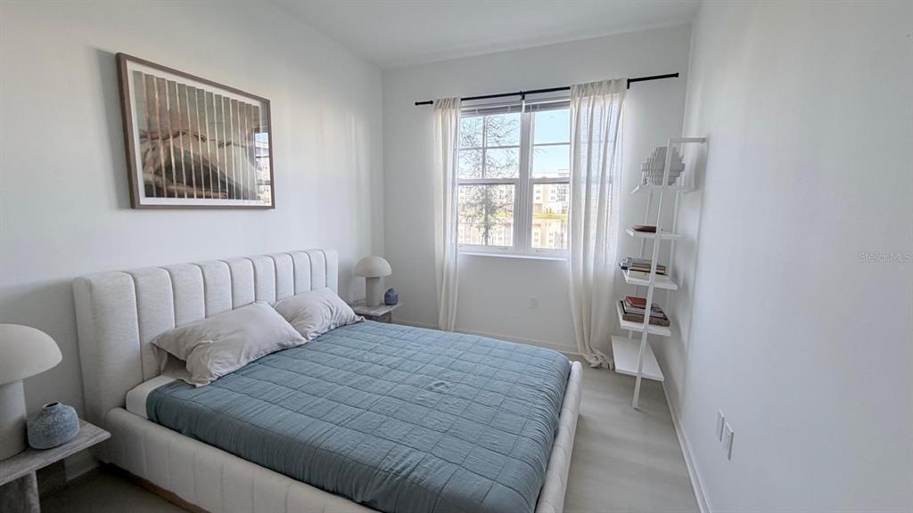 A bedroom features a bed with a blue quilt, a window, and a white bookshelf — 5587 MILLENIA PARK BLVD UNIT 210, ORLANDO, FL