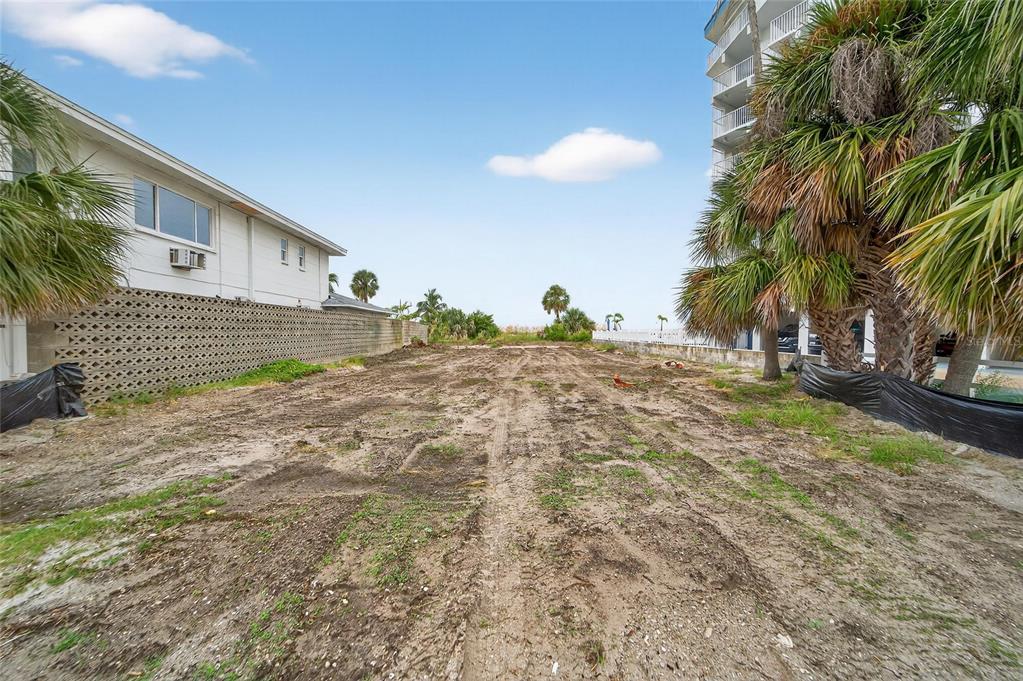 A vacant, dirt-covered lot sits between a white building and a tall residential structure — 10178 GULF BOULEVARD, TREASURE ISLAND, FL