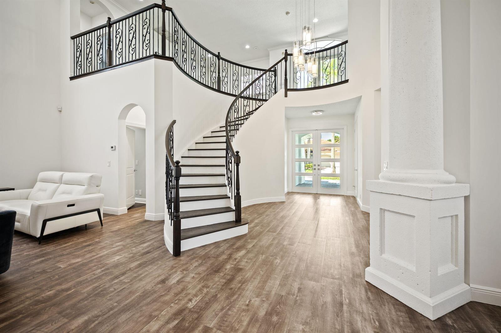 A grand foyer features a curved staircase with iron railings, light wood flooring, and white walls — 16014 Laurel Creek Drive, Delray Beach FL 33446, DELRAY BEACH, FL