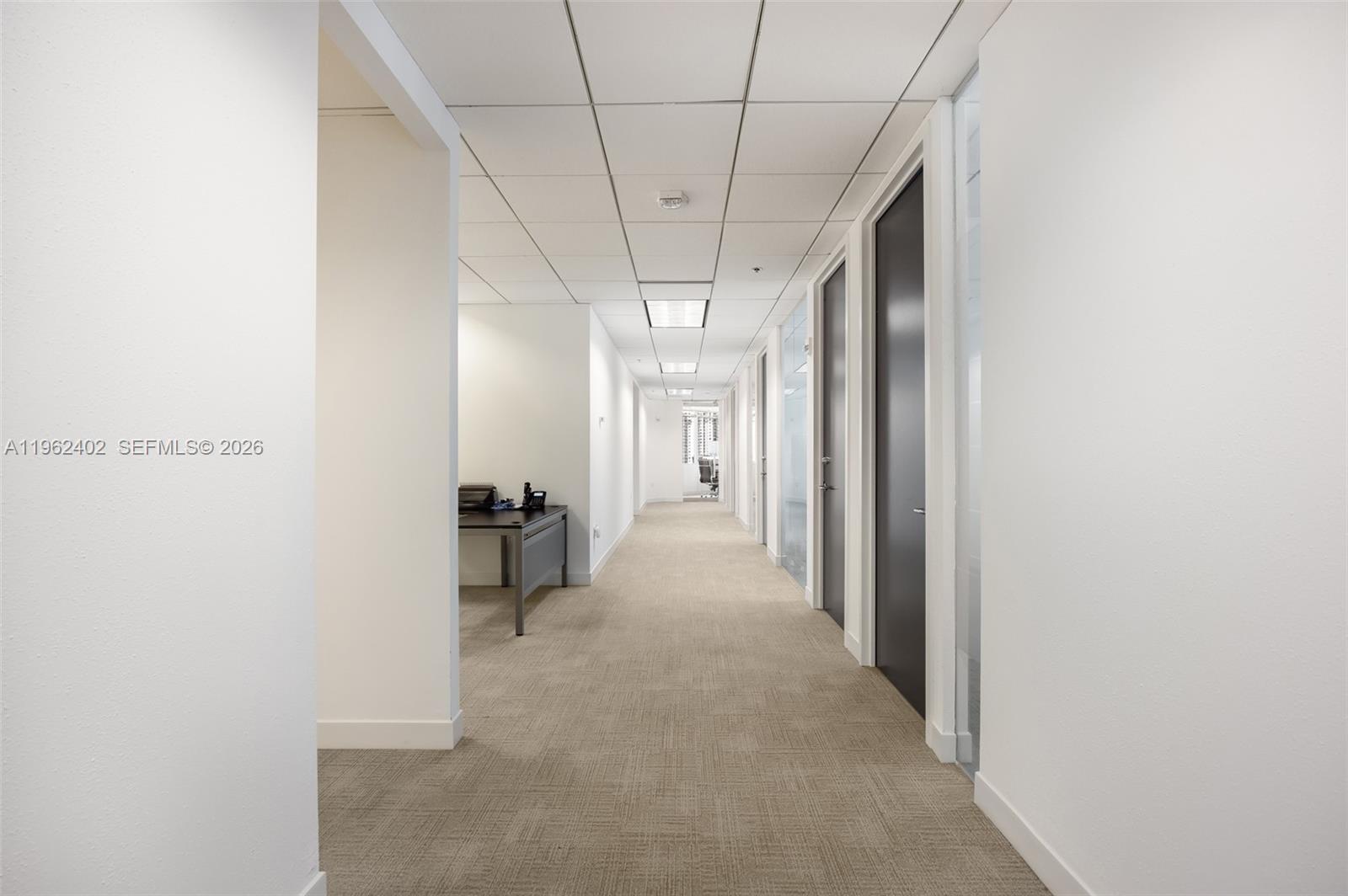 A long office hallway features beige carpet, white walls, and several dark-colored doors — 1001 Brickell Bay Dr # 2112, Miami FL 33131, MIAMI, FL