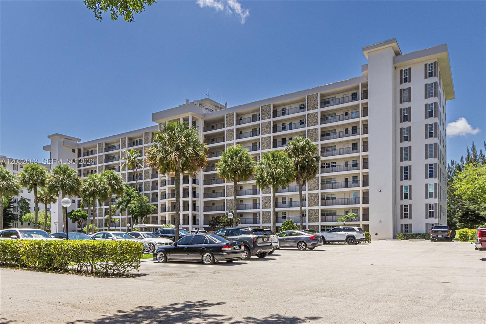 A multi-story residential building features a central driveway with landscaped hedges and palm trees — 3150 N Palm Aire Dr # 705, Pompano Beach FL 33069, POMPANO BEACH, FL