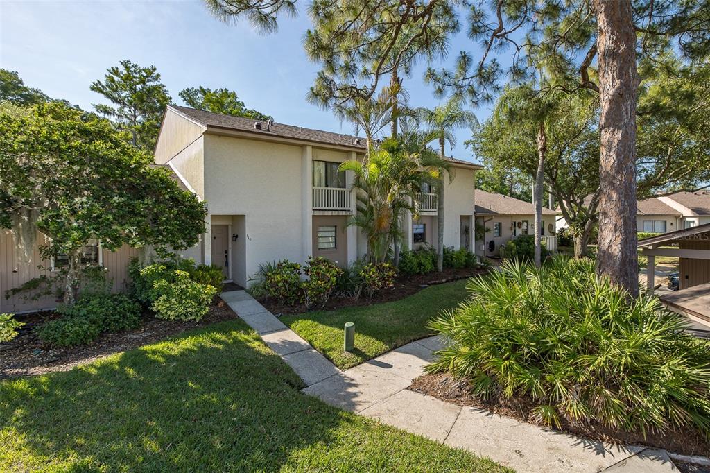 A two-story townhouse exterior with a concrete walkway, palm trees, and surrounding landscaping — 110 INGRID PLACE, OLDSMAR, FL