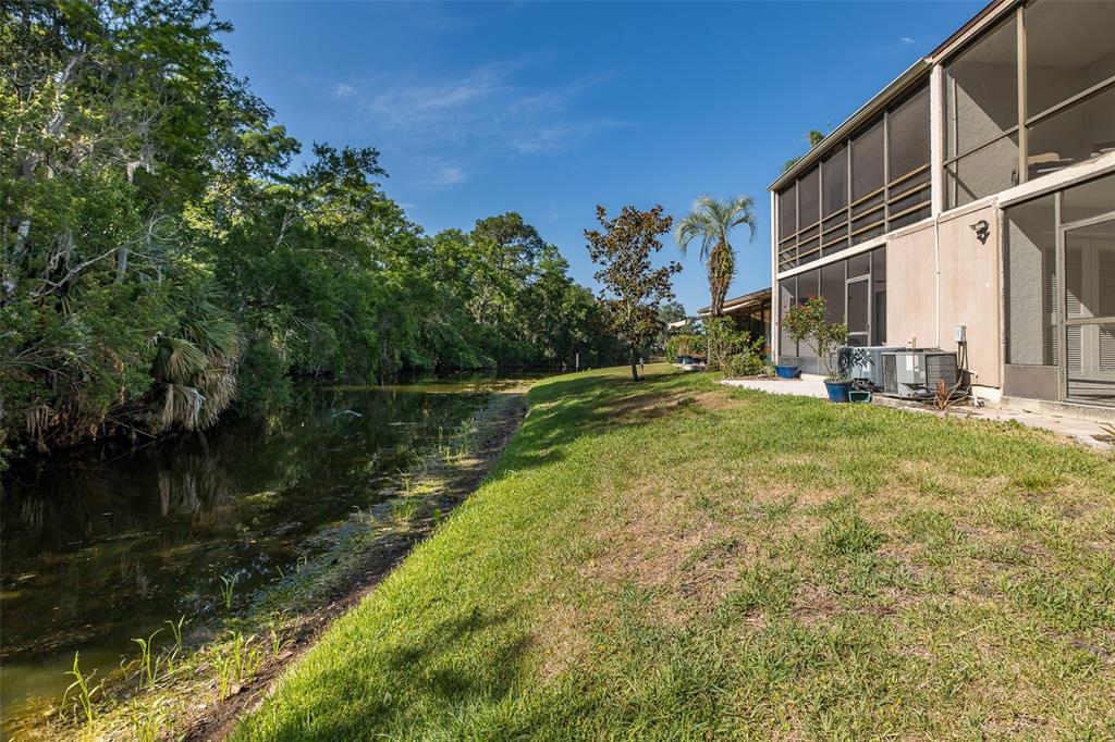 A grassy backyard borders a canal next to a house with a screened-in porch — 110 INGRID PLACE, OLDSMAR, FL