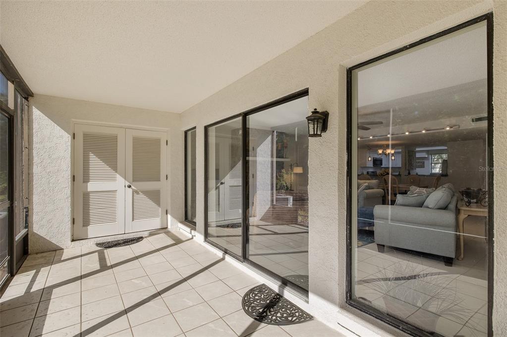 A covered patio with tiled flooring, white louvered double doors, and large glass sliding doors — 110 INGRID PLACE, OLDSMAR, FL