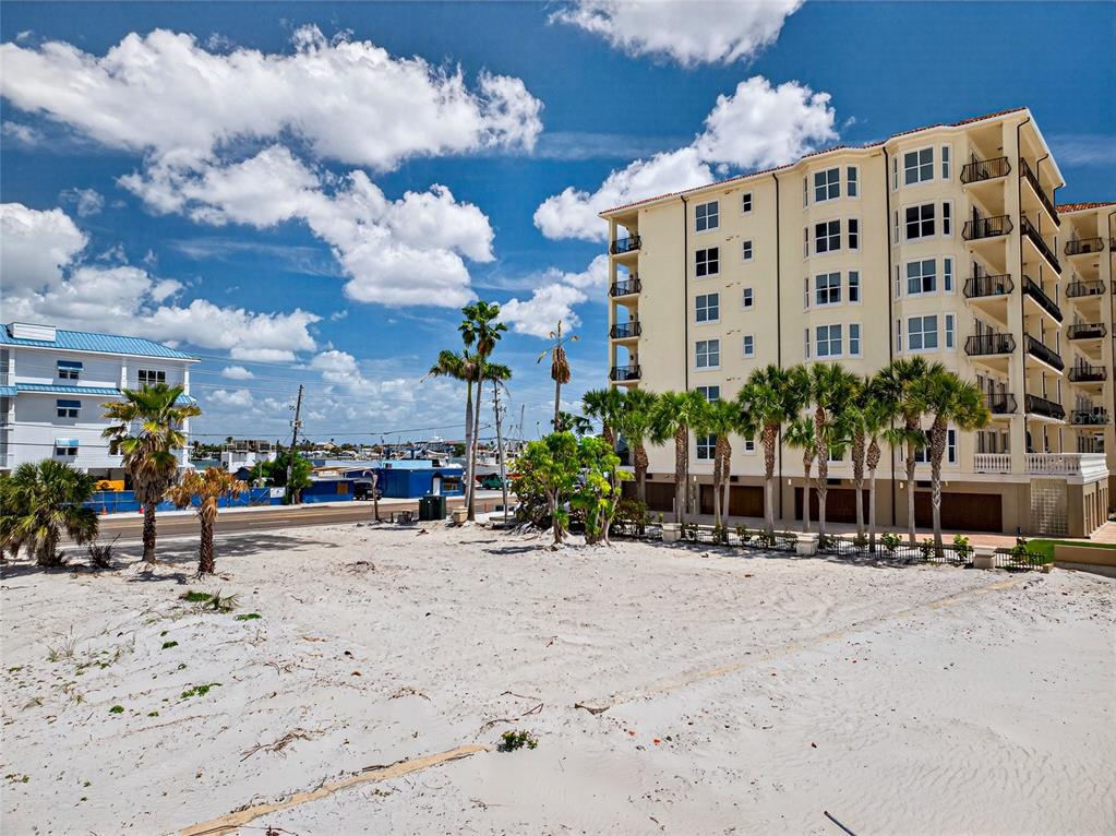 A sandy beach lot sits in front of a multi-story apartment building with palm trees — 13642 GULF BOULEVARD, MADEIRA BEACH, FL