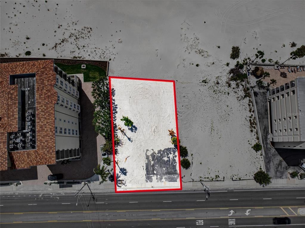 An aerial view shows a rectangular, vacant sandy lot outlined in red next to buildings — 13642 GULF BOULEVARD, MADEIRA BEACH, FL